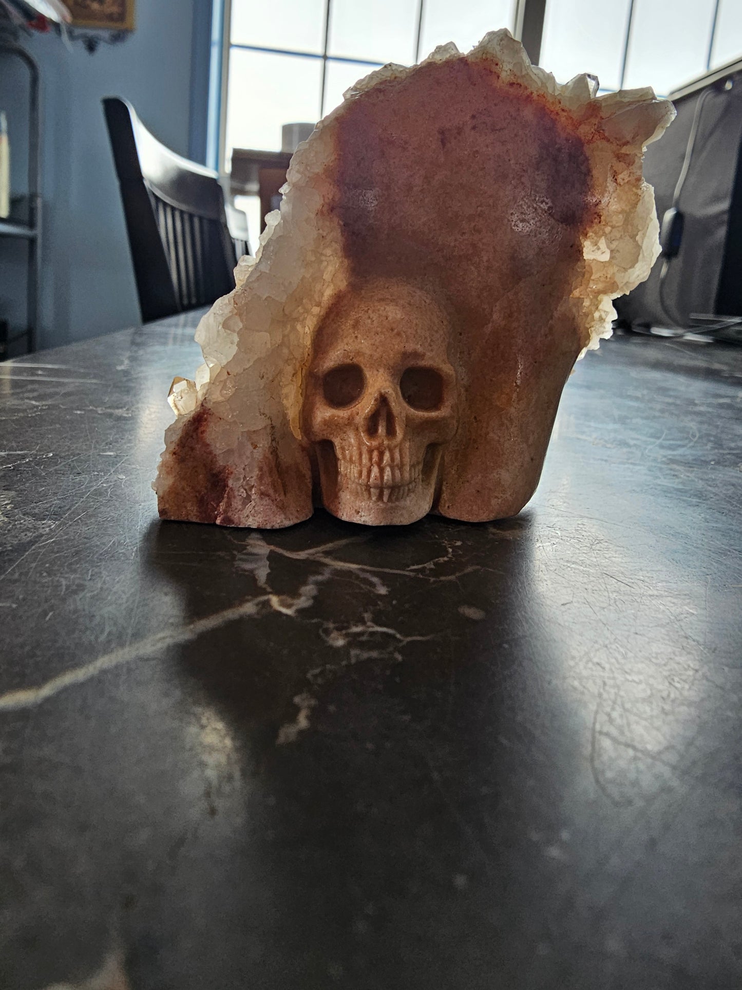 Clúster de cuarzo con calavera de sanador dorada tallada sobre matriz